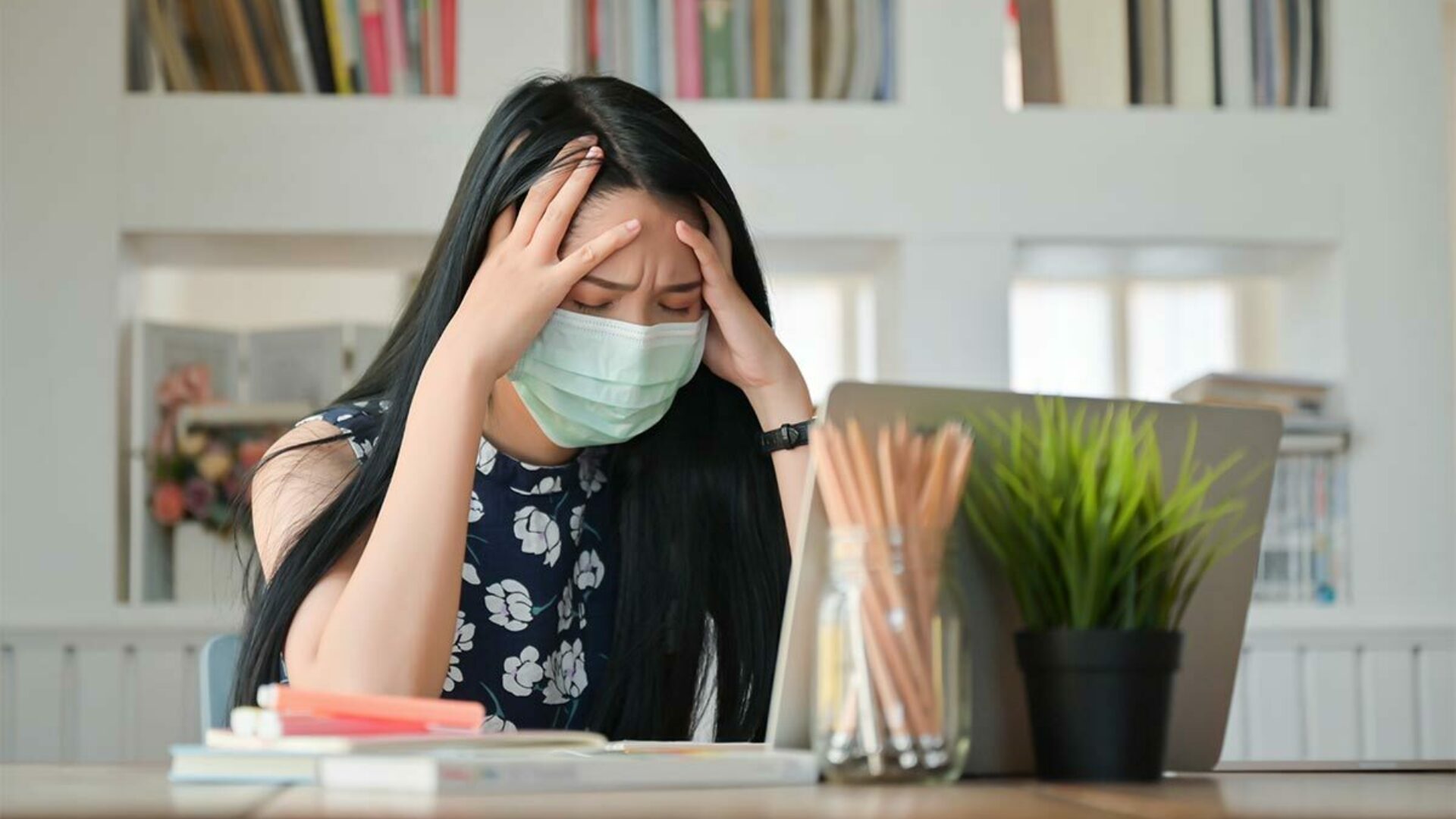 Stressed woman wearing a mask works on her computer
