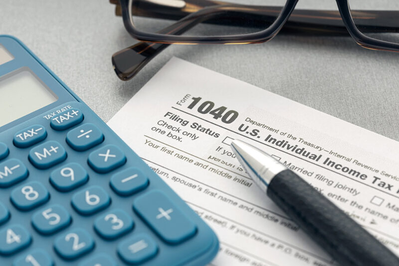 1040 tax form next to a calculator, pen, and pair of glasses