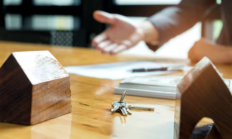 Realtor gesturing to a contract with two wooden house models infront.