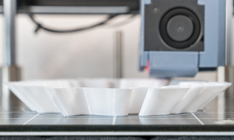 3D-printer making a wavy base to a white object.