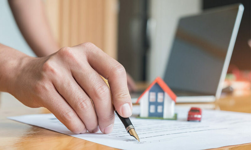 Person outlining mortgage contract with small house model on desk.