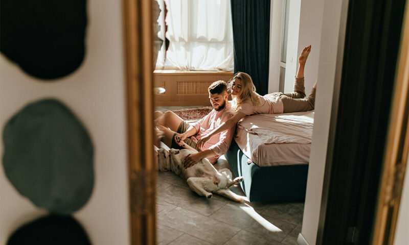 Couple playing with their dog in their bedroom.