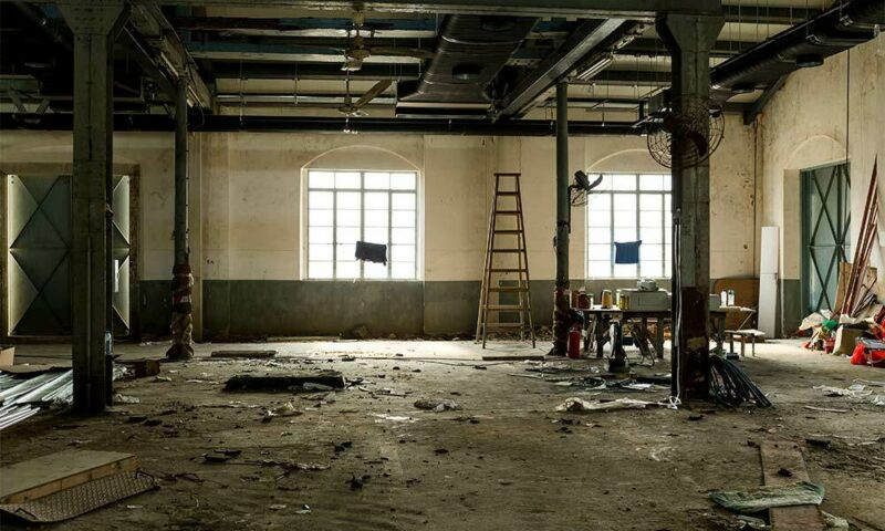 Abandoned house with 2 large windows, 4 pillars nd a ladder in the back.