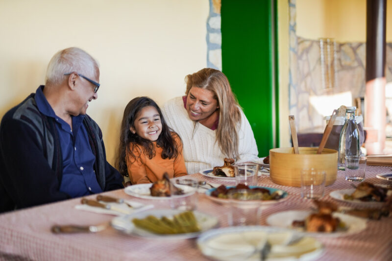 Mexican family gathering for a meal. Little girl sitting with her grandparents.