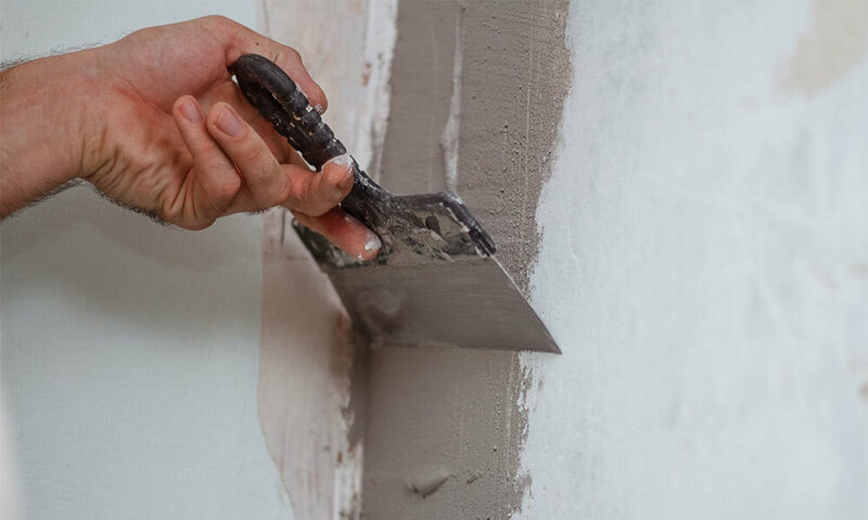 Hand using putty knife to repair crack in concrete