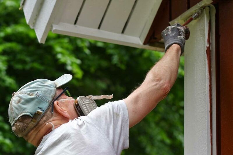 masked man painting exterior of house