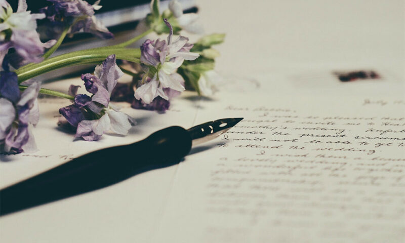 Quill pen on top of love letter with purple flowers next to it.
