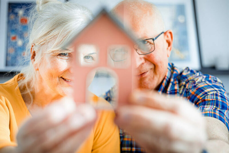 senior couple holding a model of a house looking through the windows