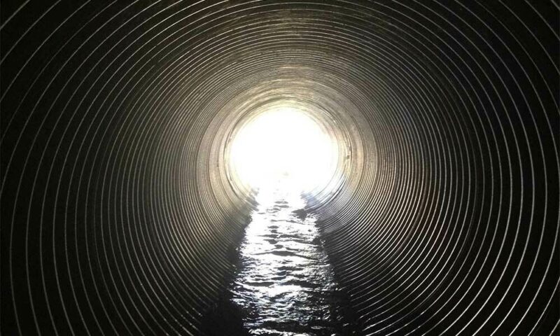 View through sewage tunnel with light at the end.