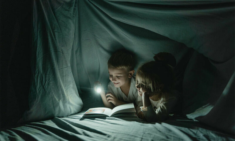 Kids reading a book under a blanket fort.